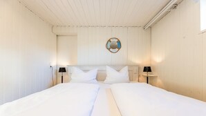 Un lit double avec du linge de lit blanc, deux lampes de chevet et un panneau circulaire de bienvenue accroché au mur.