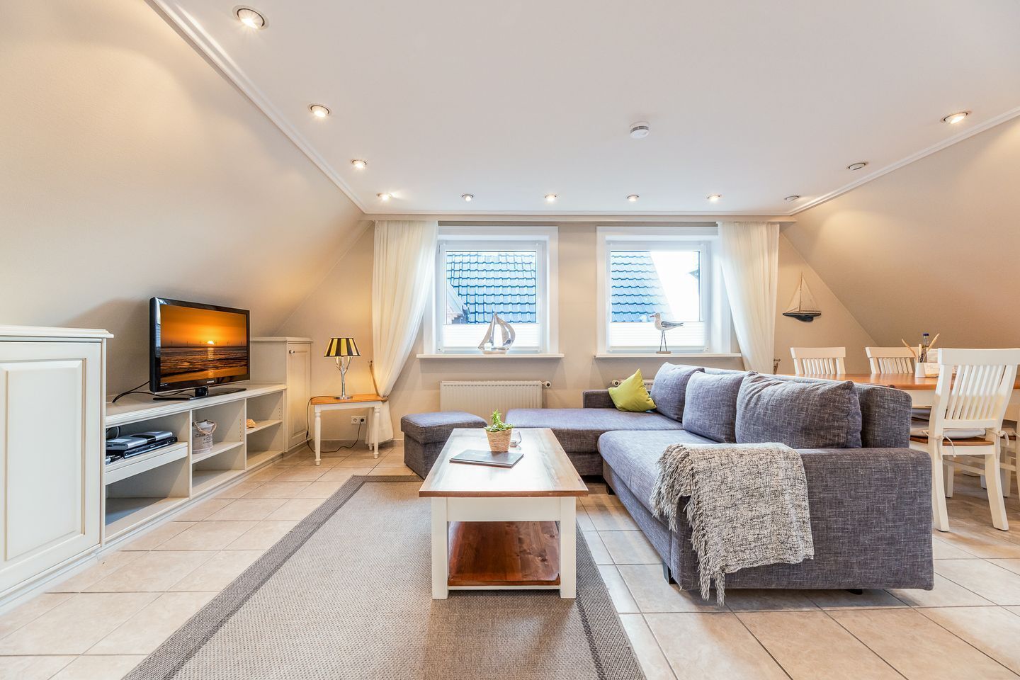 A modern living room with a flat-screen TV, a sofa, a coffee table, and a dining area with chairs and a table.