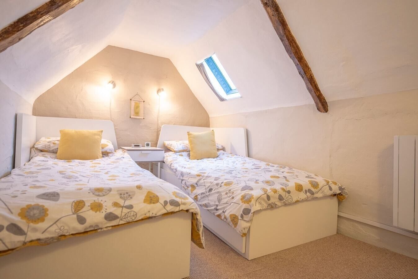 A cozy attic bedroom with two beds, a small desk, and a window.