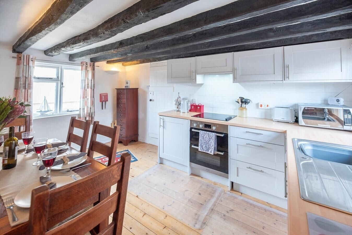 A modern kitchen with white cabinets, a wooden dining table, and a built-in oven.
