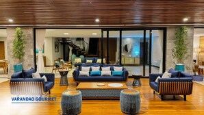 A spacious living area with a modern design, featuring a large sofa set, wooden flooring, and two large potted plants. - Casa Beira-mar com 8 Suítes no Prestigiado Condomínio Iberostar - Praia do Forte (Açu da Torre)