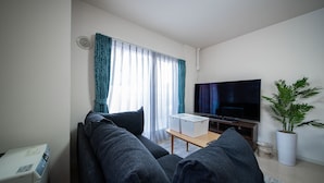 En opholdsstue med sofa, fjernsyn, et lille bord og en potteplante.