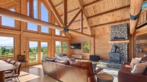 A spacious log cabin interior with a large fireplace, leather seating, and a dining area with a view of the outdoors. - Mountain Majesty: Timber Lodge with Stunning Views (Morristown)