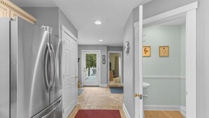 A kitchen with a stainless steel refrigerator, a hallway with a red rug, and a bathroom with a sink and toilet. - Gorgeous 3 bedroom in popular Stowe location. (Stowe)
