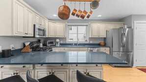 A kitchen with white cabinetry, a central island, stainless steel appliances, and hanging pots. - Gorgeous 3 bedroom in popular Stowe location. (Stowe)