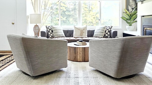 Una sala de estar moderna con dos sillones grises, una mesa de centro redonda y un ventanal con vistas a árboles.