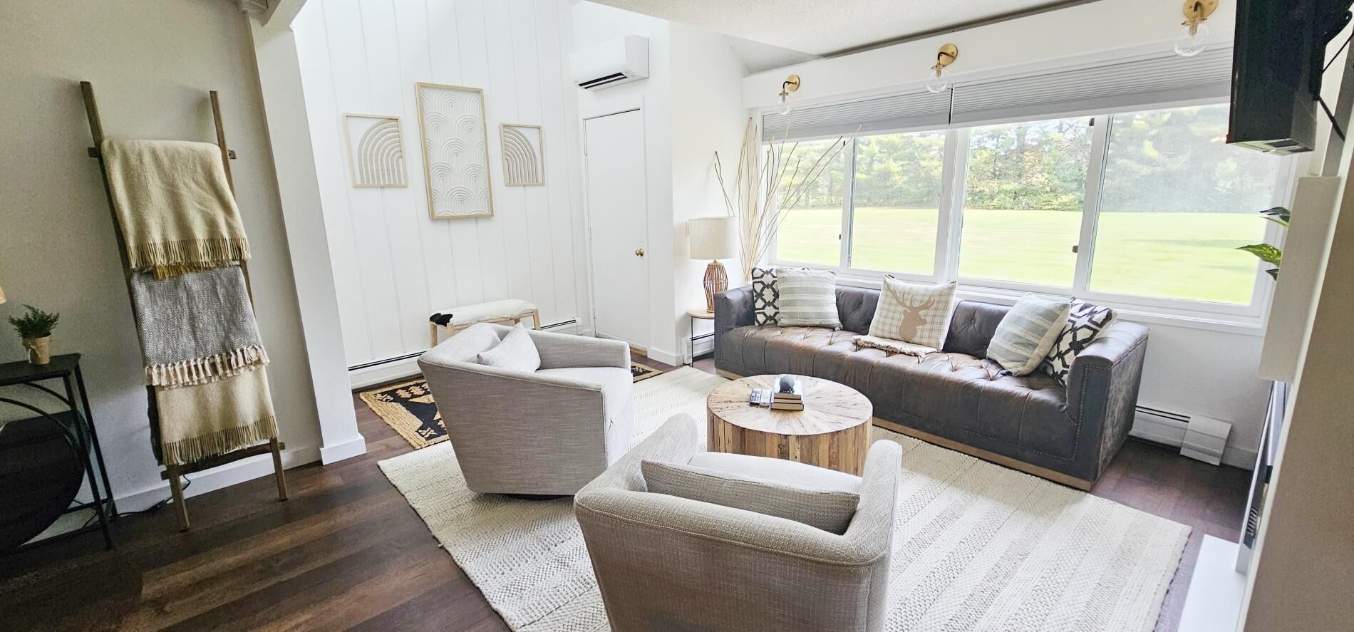 A living room with a sofa, armchairs, a coffee table, and a view of a garden through a large window.