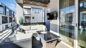 Une terrasse extérieure dotée d’une table à plateau de verre, de meubles en osier et d’un téléviseur à écran plat fixé au mur.