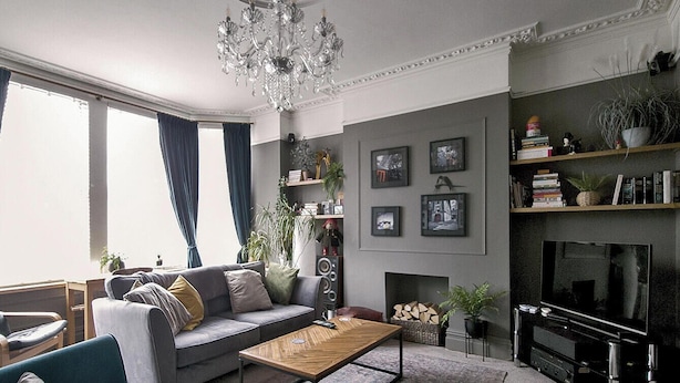 A living room with a sofa, armchair, coffee table, and a fireplace. There are bookshelves and a chandelier.