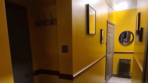 A hallway with yellow walls, a radiator, a door, and a mirror on the wall.