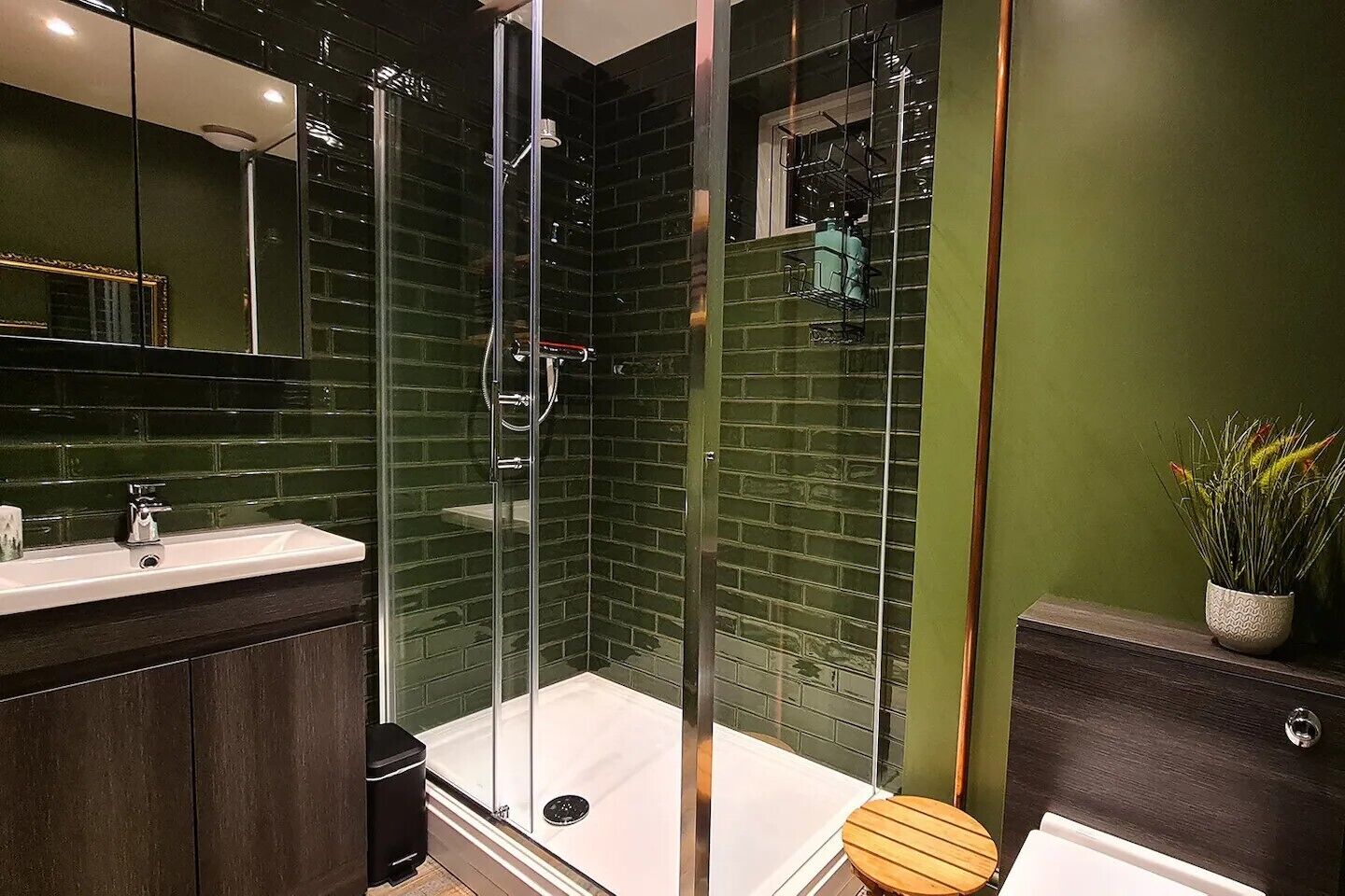 Une salle de bain moderne avec une douche à parois de verre, des murs vert foncé et un meuble-lavabo en bois.