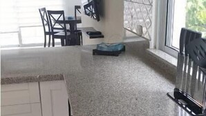 Eine Küche mit weißen Schränken, einer Arbeitsplatte aus Granit und einem Fenster mit Jalousien.