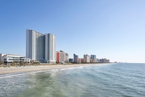 A coastal cityscape with high-rise buildings, a beach, and clear skies.