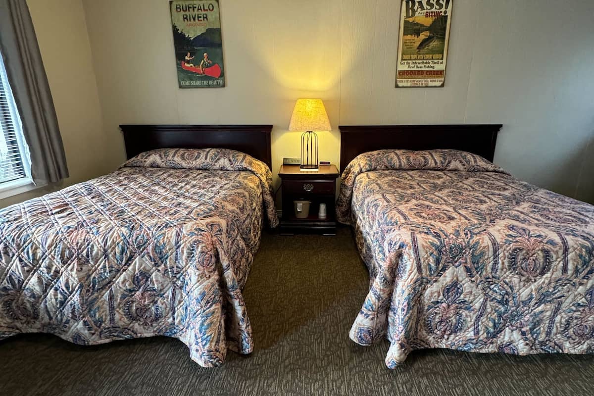 Una habitación de hotel con dos camas, una mesita de noche con lámpara y dos carteles en la pared.