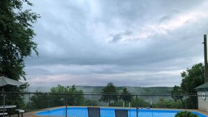 Une piscine extérieure offrant une vue sur le paysage environnant, une zone délimitée par une clôture et quelques chaises longues.