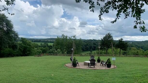 Un espace extérieur circulaire aménagé avec des chaises et des tables, entouré d’un champ d’herbe et d’arbres.