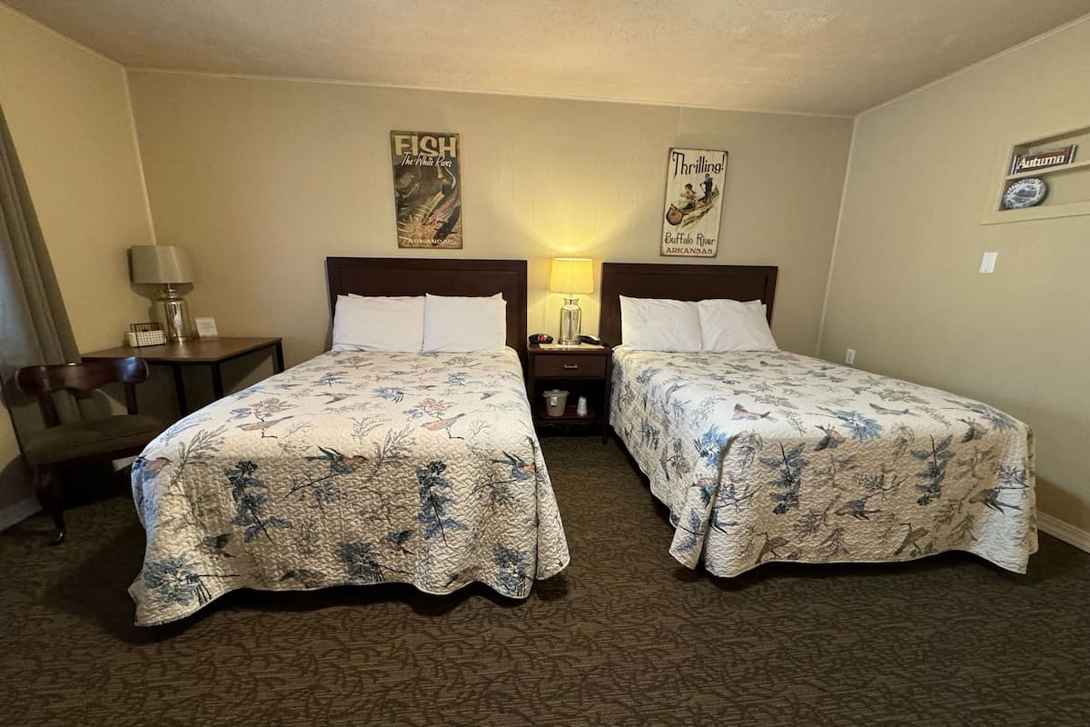 Habitación de hotel con dos camas, un escritorio, una silla y una mesita de noche con lámpara.