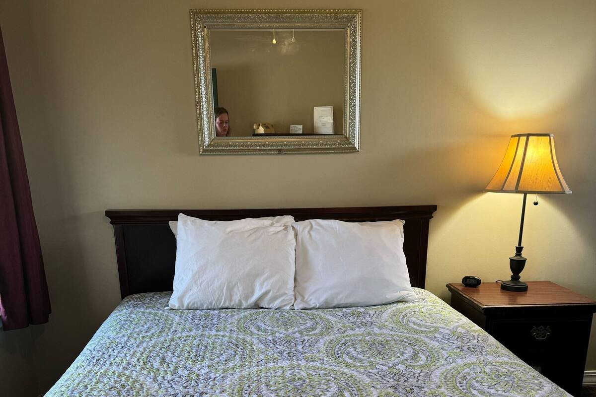 Una habitación de hotel con una cama grande, una mesita de noche con lámpara, un espejo y un reloj de pared.