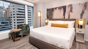 A hotel room with a large bed, a green armchair, a small table, and a city view. - NYC | 5th Ave Location | Central Park | Studio Penthouse (New York)