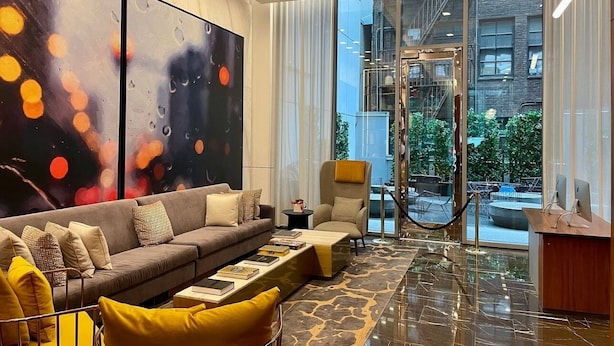 A modern living room with a sofa, armchair, and coffee table, large abstract paintings, and a view of the city through large windows. - NYC | 5th Ave Location | Central Park | Studio Penthouse (New York)