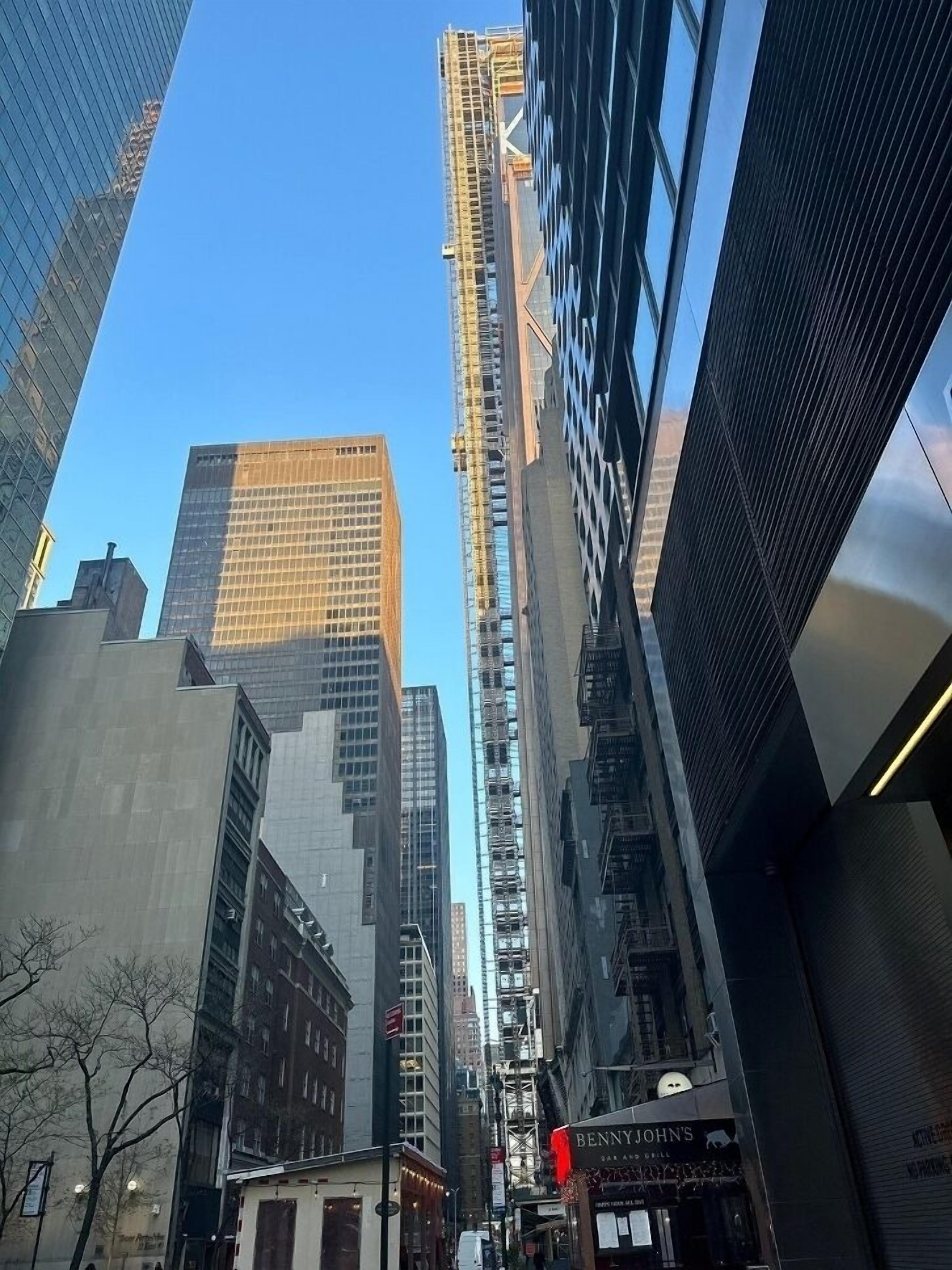 A cityscape with tall buildings, including a construction site on one of the skyscrapers.