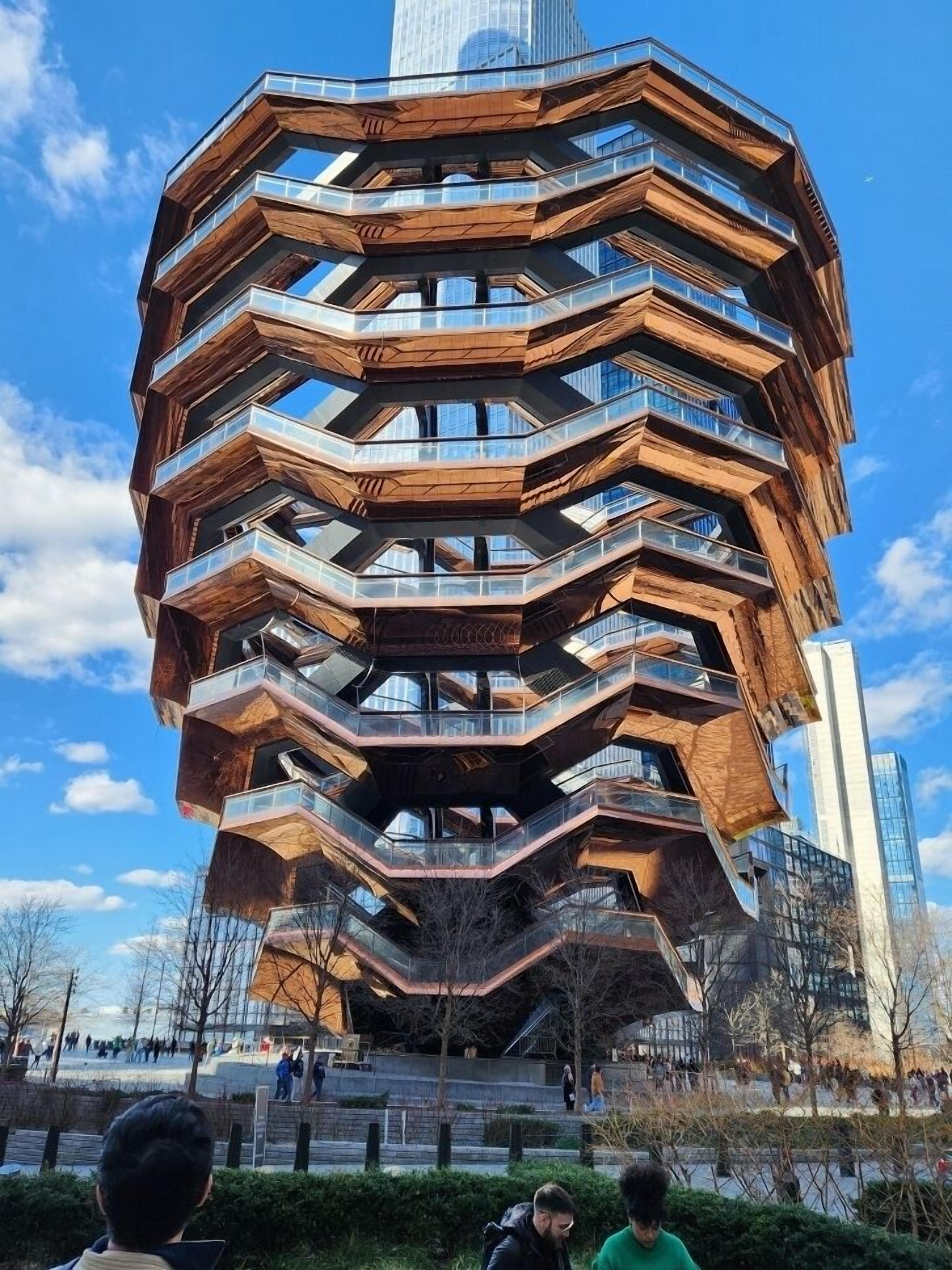 Un bâtiment aux lignes angulaires, composé de plusieurs niveaux et doté de balcons, entouré d’une place publique animée.