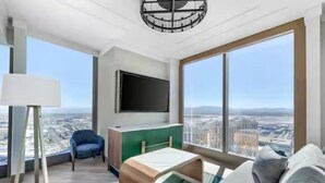 A modern living room with a large window, a flat-screen TV, a sofa, a chair, and a small table. - Las Vegas | Luxury City Retreat | Pool + Gym (Las Vegas)