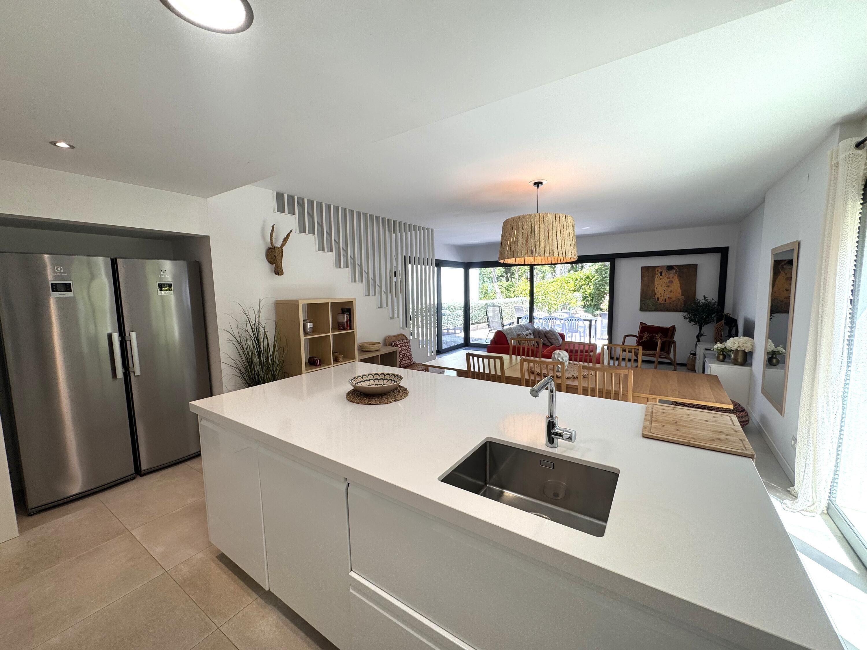 Een moderne keuken met een centraal eiland, roestvrijstalen apparatuur en een eethoek met een rode bank en houten meubels.