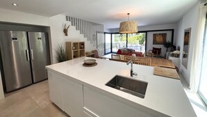 A modern kitchen with a central island, stainless steel appliances, and a dining area with a red sofa and wooden furniture. - VILLA BRASIL  - villa with communal area - Llafranc-Costa Brava (Llafranc)