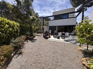 A modern outdoor patio with seating and a grill area, surrounded by well-maintained gardens and trees.