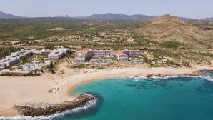 An aerial view of a coastal resort with multiple buildings, a sandy beach, and turquoise waters. - Los Cabos | Elevated Coastal Retreat | Pool + Beach (Cabo del Sol)