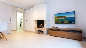 A modern living room with a fireplace, a wooden cabinet, and a large window with a scenic view. - CAPDEVILA 9 (Llafranc)