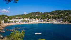 A coastal town with a beach, boats, and buildings on hills. - CAPDEVILA 9 (Llafranc)