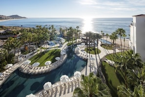 A resort with a large pool, palm trees, and a view of the ocean.