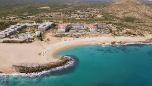 An aerial view of a coastal resort with multiple buildings, a sandy beach, and turquoise waters.