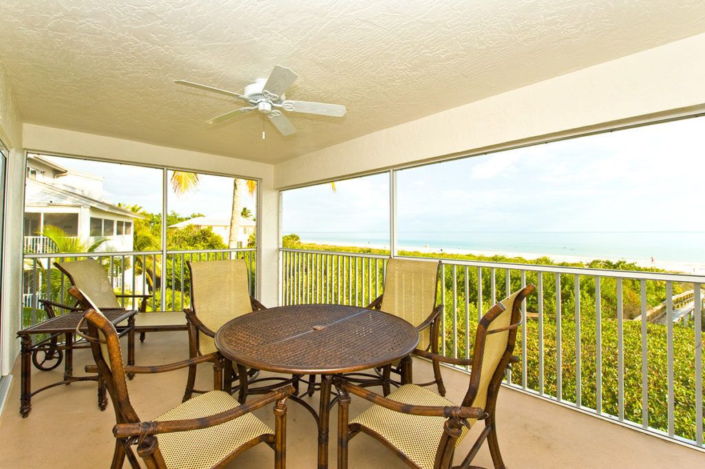 Ein Balkon mit rundem Tisch und Stühlen, einem Deckenventilator und Blick aufs Meer.
