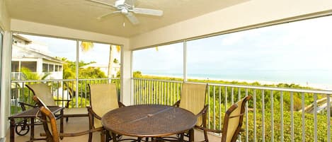 Ein Balkon mit rundem Tisch und Stühlen, einem Deckenventilator und Blick aufs Meer.