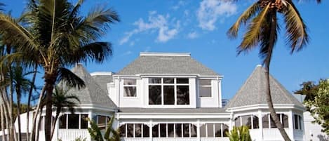 A large white building with a gabled roof and multiple windows, surrounded by palm trees.