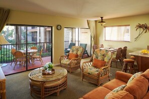 Un amplio salón con mobiliario de mimbre, una mesa de comedor y un balcón con vista a palmeras.