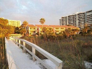 A beachfront hotel with a white walkway leading to the buildings, surrounded by palm trees and a sandy beach. - Marco Island | Family Beach Getaway | Pool + Beach | 2BR (Marco Island)