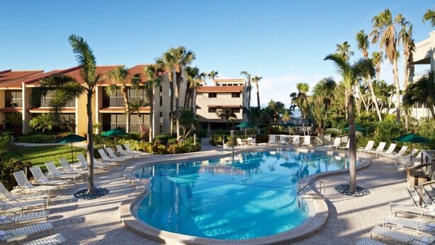 A resort pool area with lounge chairs and palm trees. - Marco Island | Family Beach Getaway | Pool + Beach | 2BR (Marco Island)