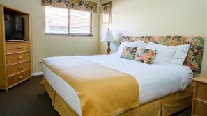 Una habitación de hotel con cama, cómoda de madera, televisor y ventana con persianas.
