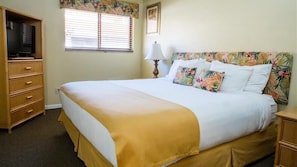 Una habitación de hotel con cama, cómoda de madera, televisor y ventana con persianas.