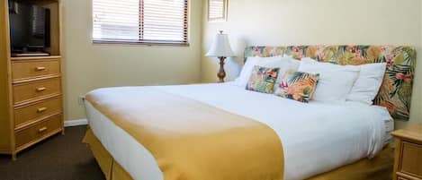 Une chambre d’hôtel avec un grand lit, une commode, une télévision et une fenêtre avec des stores.