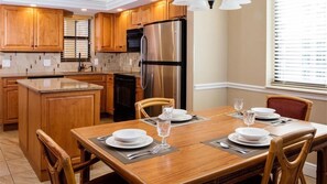 Una cocina moderna con armarios de madera, un refrigerador de acero inoxidable y un comedor con una mesa de madera dispuesta para cuatro.
