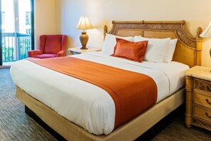 Un cuarto de hotel con una cama grande, un sillón rojo, una mesita de noche con lámpara y vistas al exterior.