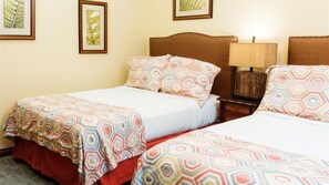 A hotel room with two beds, each with patterned bedding, a nightstand with a lamp, and framed artwork on the wall.