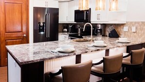 A kitchen with a granite countertop, stainless steel appliances, and bar stools.