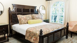 A bed with a patterned bedspread, a bedside table, a chair, and a window with curtains.
