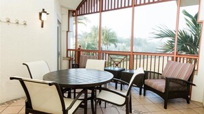 A dining area with a round table and chairs, a small table with a chair, and a view through a large window.